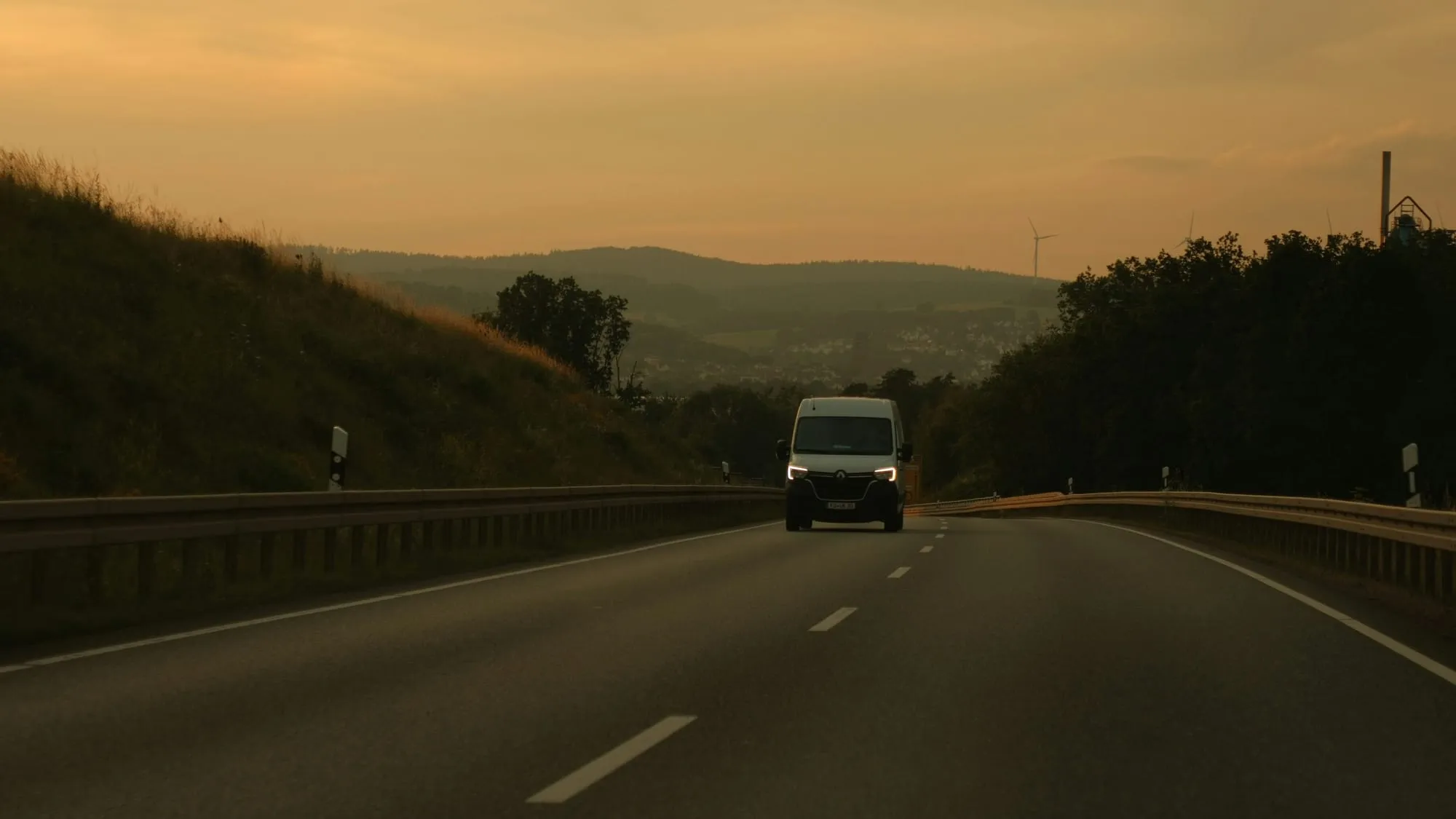Fourgon utilitaire blanc sur une route de campagne au coucher du soleil, collines à l'horizon